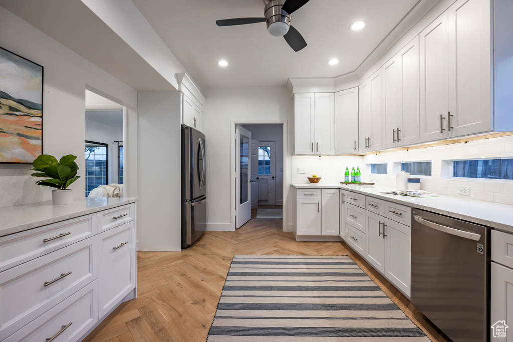 Kitchen featuring appliances with stainless steel finishes, white cabinets, decorative backsplash, light parquet flooring, and ceiling fan