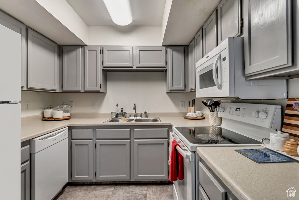 Kitchen with gray cabinetry, sink, light tile flooring, and white appliances