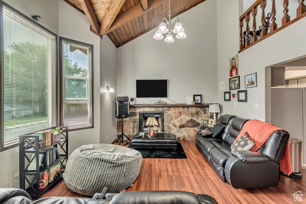 Living room with an inviting chandelier, wooden ceiling, hardwood / wood-style floors, a stone fireplace, and beam ceiling