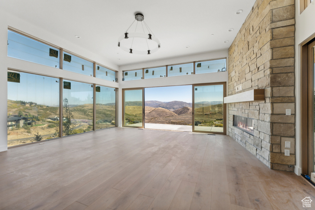 Unfurnished living room with a stone fireplace, light hardwood / wood-style floors, a mountain view, and a towering ceiling