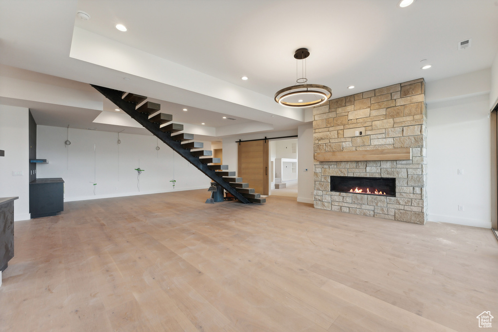 Unfurnished living room with light hardwood / wood-style floors, a barn door, and a stone fireplace