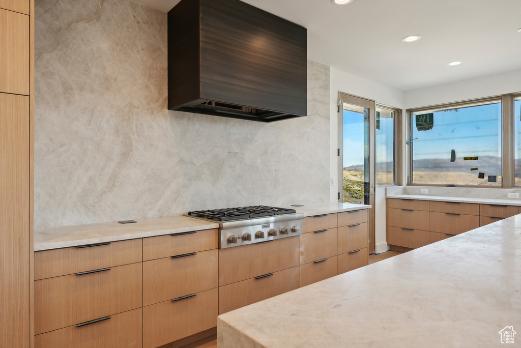 Kitchen with light brown cabinets, exhaust hood, backsplash, light hardwood / wood-style flooring, and stainless steel gas cooktop