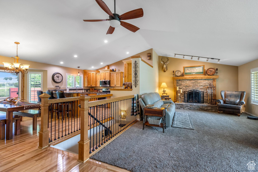 Living room featuring light carpet, vaulted ceiling, a fireplace, ceiling fan with notable chandelier, and rail lighting