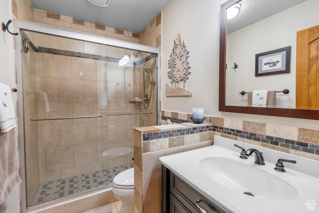 Bathroom featuring toilet, tile floors, tasteful backsplash, a shower with shower door, and vanity