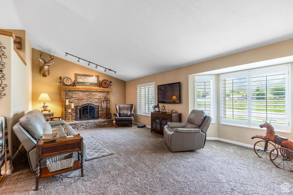 Carpeted living room with track lighting, a stone fireplace, and vaulted ceiling