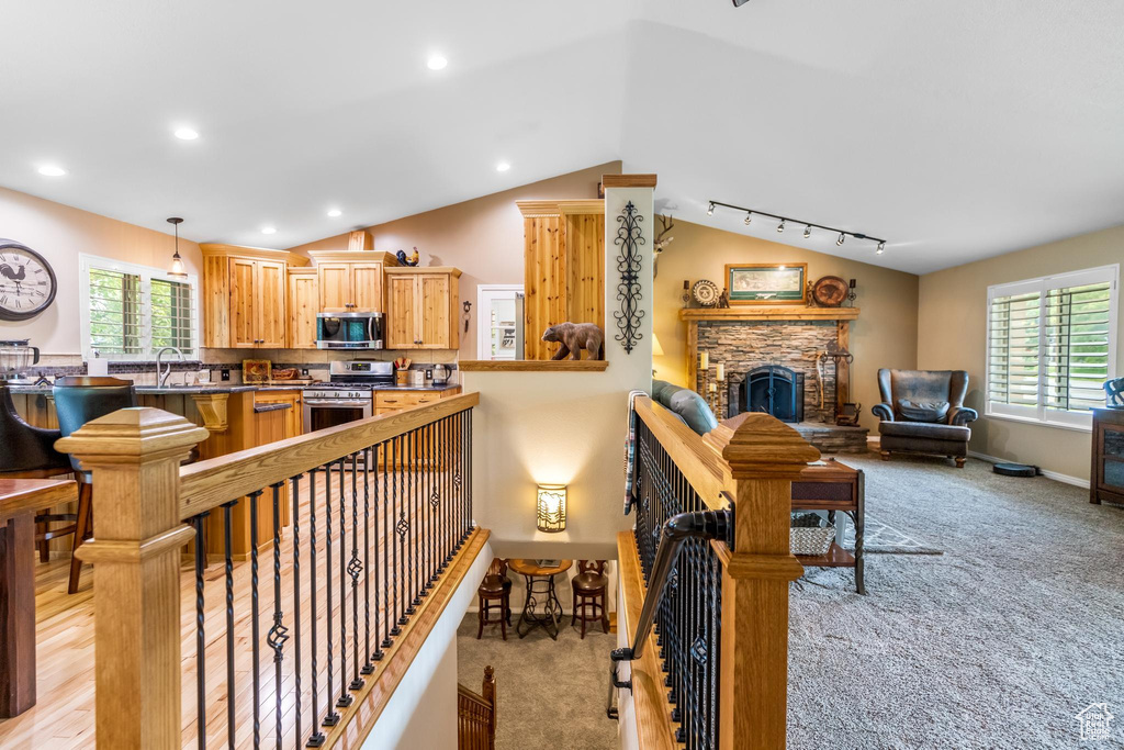 Interior space with a stone fireplace, light hardwood / wood-style flooring, track lighting, sink, and lofted ceiling