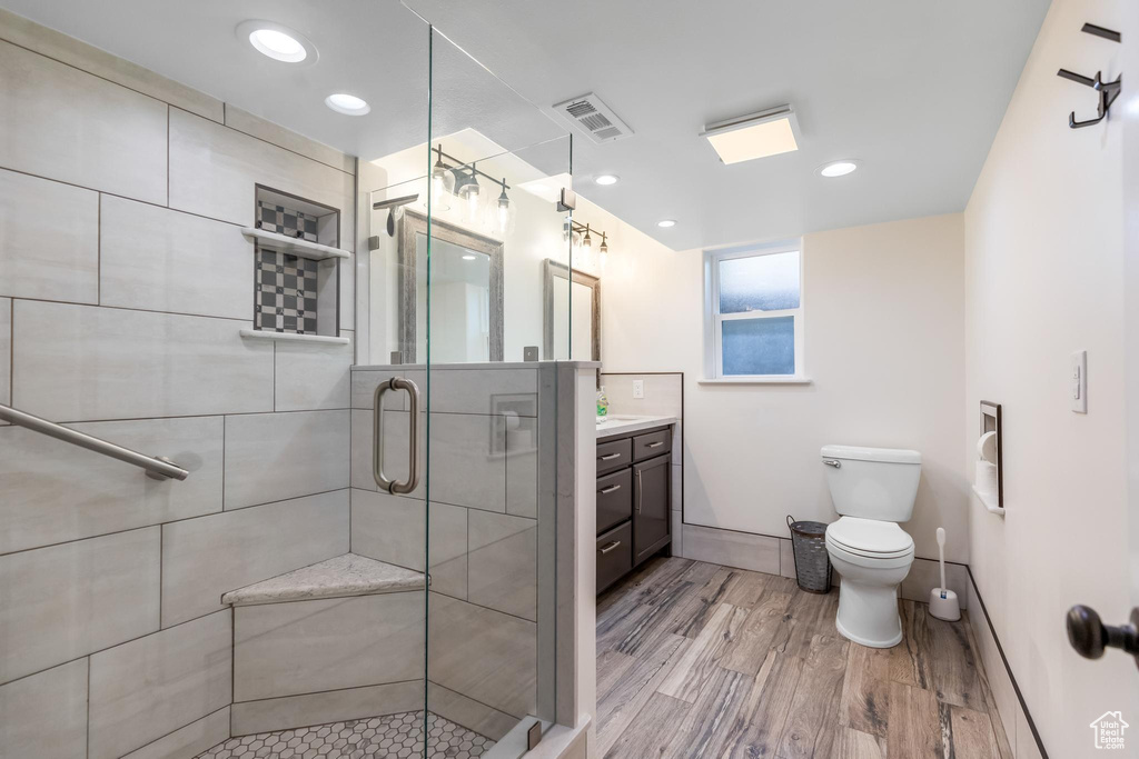 Bathroom featuring hardwood / wood-style floors, walk in shower, vanity, and toilet