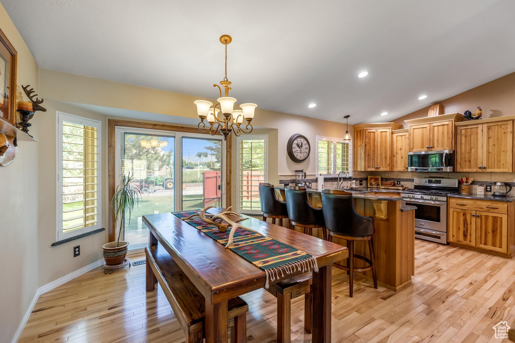 Dining room featuring lofted ceiling, plenty of natural light, light wood-type flooring, and an inviting chandelier