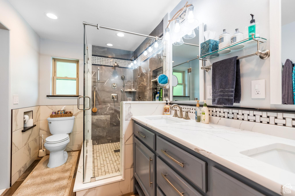 Bathroom featuring tasteful backsplash, dual vanity, an enclosed shower, tile walls, and toilet