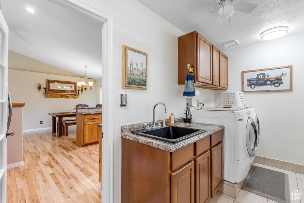 Clothes washing area featuring cabinets, light hardwood / wood-style flooring, ceiling fan with notable chandelier, separate washer and dryer, and sink