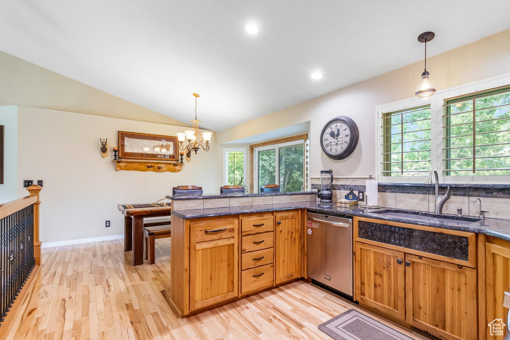 Kitchen featuring light hardwood / wood-style flooring, kitchen peninsula, stainless steel dishwasher, vaulted ceiling, and pendant lighting