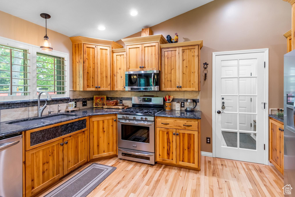 Kitchen with light hardwood / wood-style floors, stainless steel appliances, tasteful backsplash, dark stone countertops, and sink