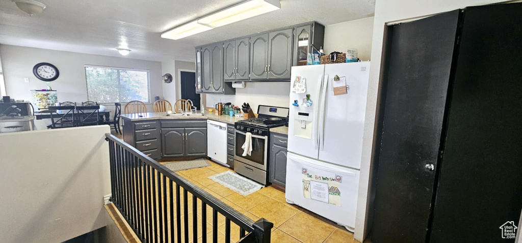 Kitchen featuring gray cabinets, sink, light tile patterned floors, and white appliances