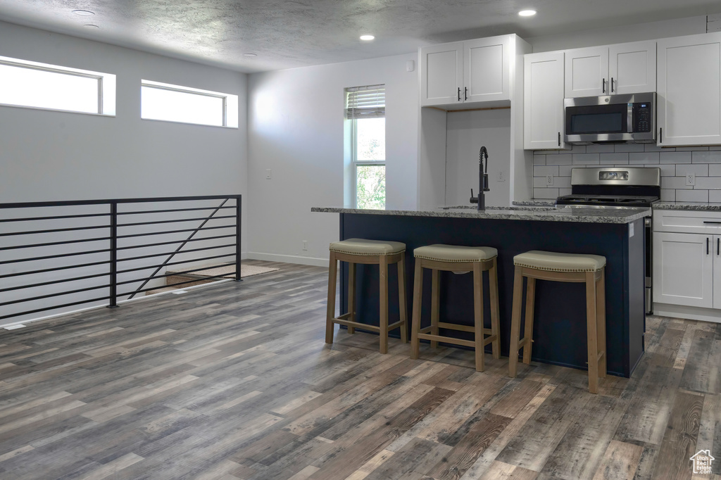 Kitchen with an island with sink, white cabinets, dark hardwood / wood-style floors, and dark stone countertops