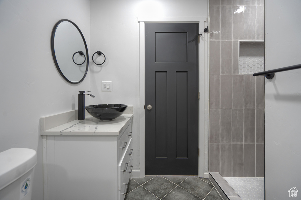 Bathroom featuring tiled shower, tile flooring, vanity, and toilet