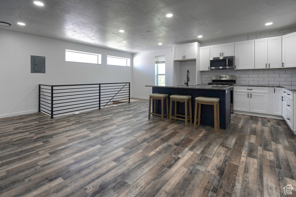 Kitchen featuring white cabinets, dark hardwood / wood-style flooring, a kitchen bar, and a kitchen island with sink