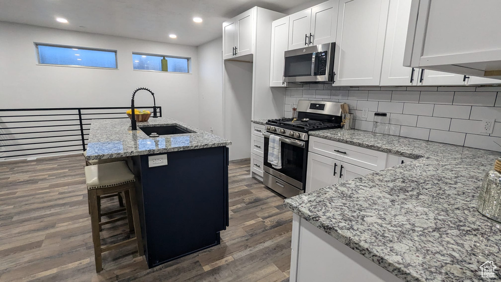 Kitchen with white cabinetry, stainless steel appliances, sink, and light stone counters