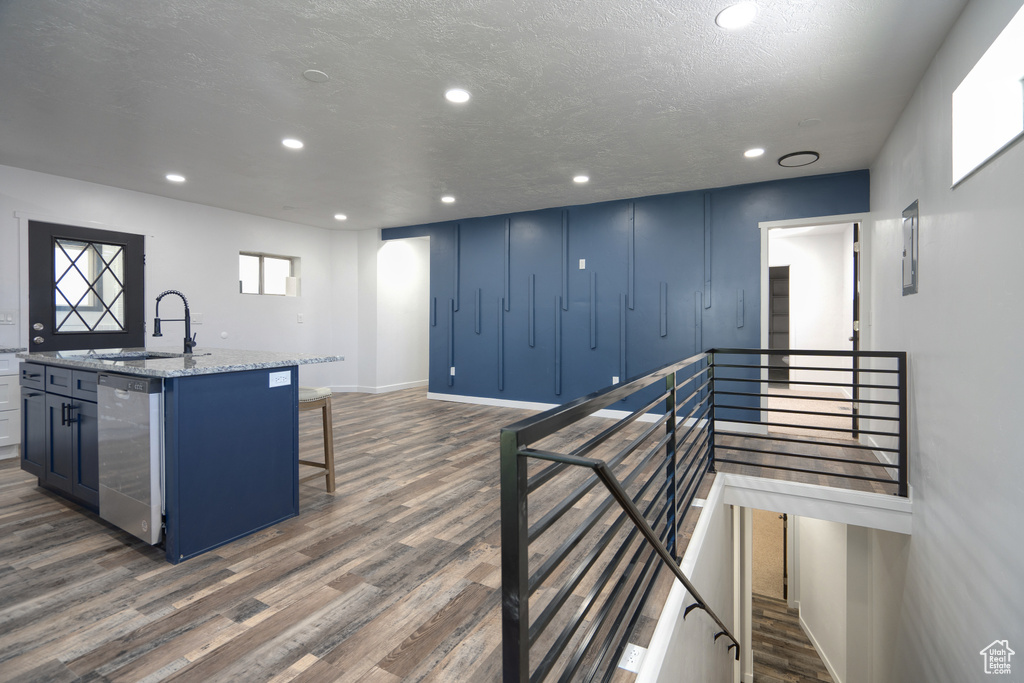 Kitchen with stone counters, hardwood / wood-style flooring, a kitchen island with sink, stainless steel dishwasher, and sink