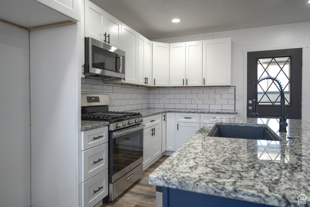 Kitchen featuring white cabinets, appliances with stainless steel finishes, dark hardwood / wood-style floors, and light stone counters