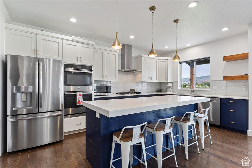 Kitchen featuring stainless steel appliances, pendant lighting, backsplash, wall chimney exhaust hood, and white cabinetry