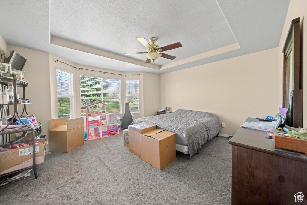 Bedroom with a textured ceiling, carpet flooring, ceiling fan, and a raised ceiling