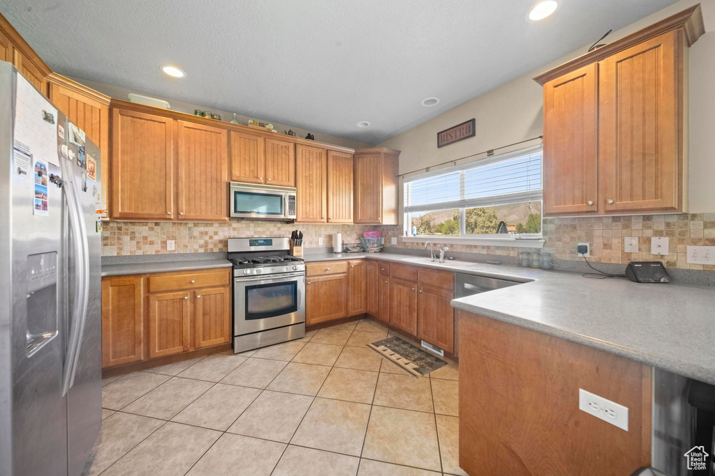 Kitchen with sink, backsplash, light tile floors, and stainless steel appliances