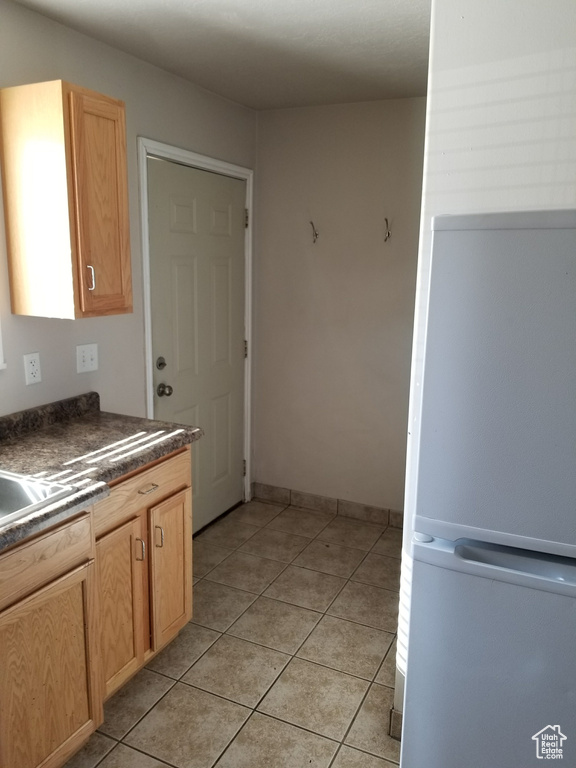 Kitchen featuring light brown cabinets, white refrigerator, and light tile floors