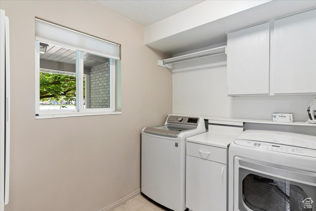 Laundry room with washing machine and dryer, cabinets, and light tile floors