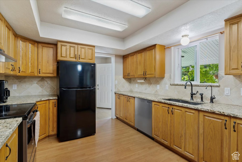 Kitchen featuring black refrigerator, light wood-type flooring, stainless steel dishwasher, and tasteful backsplash