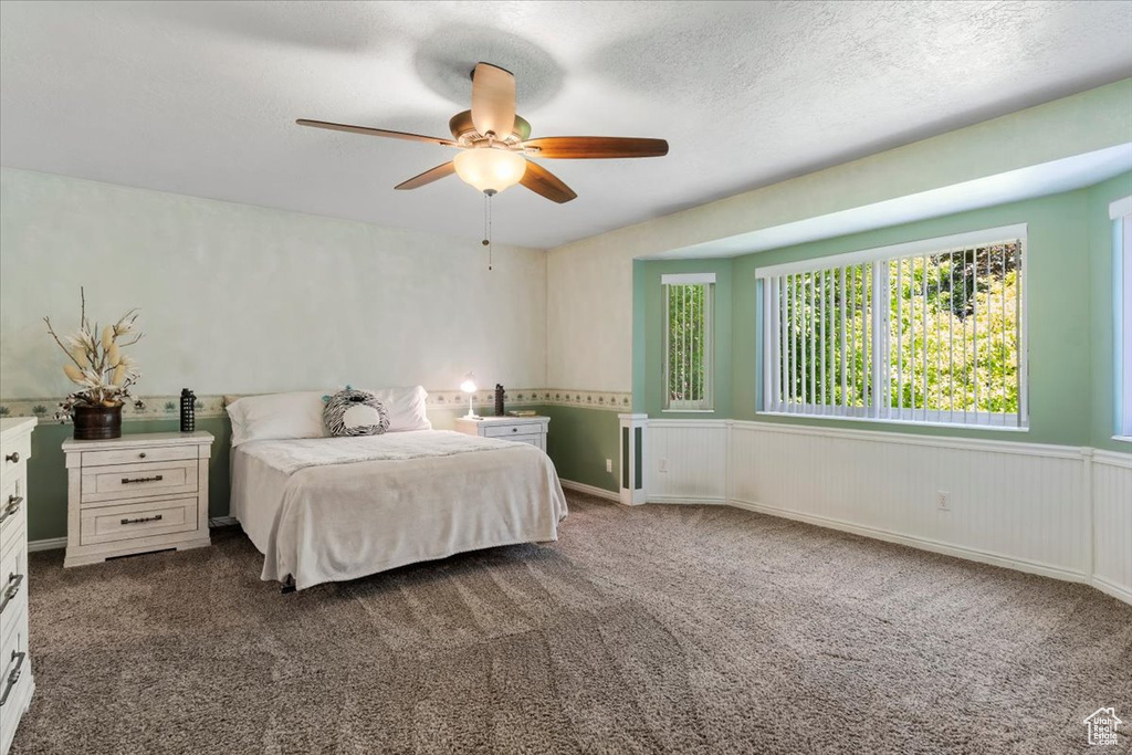 Bedroom with dark carpet, ceiling fan, and a textured ceiling