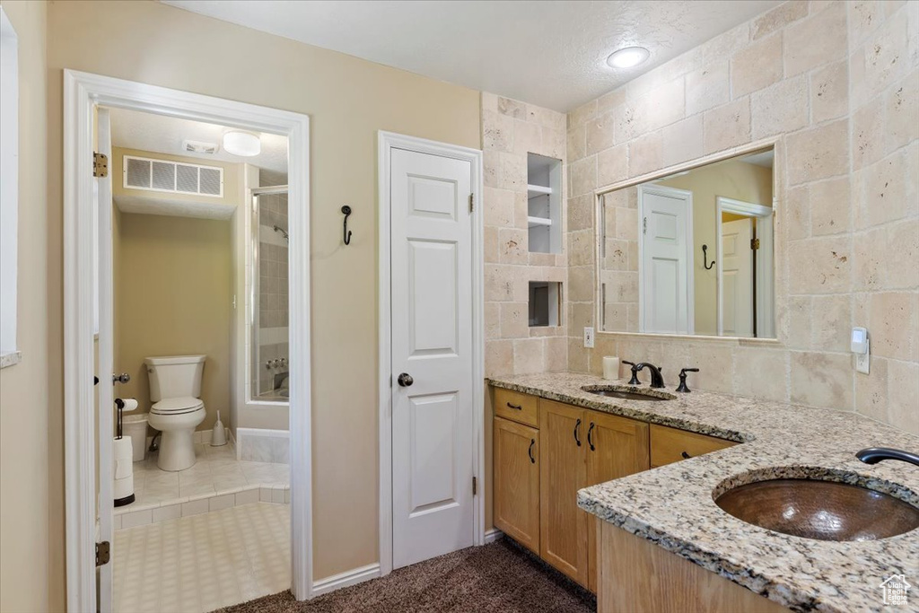 Bathroom with tile walls, tile flooring, vanity, and toilet