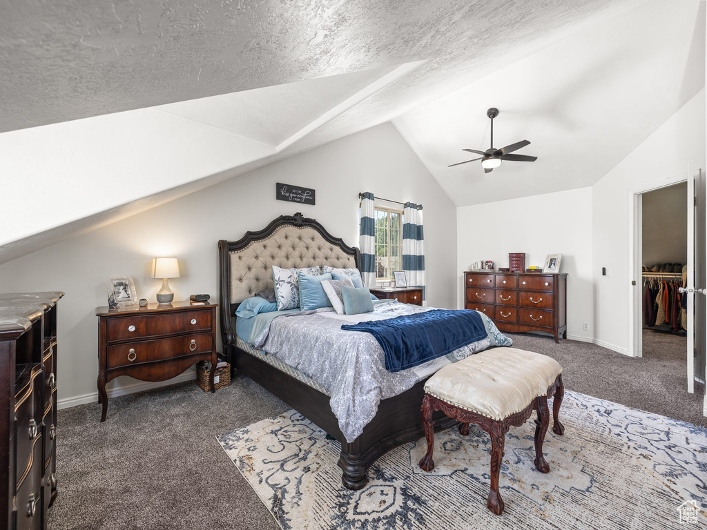 Carpeted bedroom with ceiling fan, a closet, vaulted ceiling, a textured ceiling, and a walk in closet