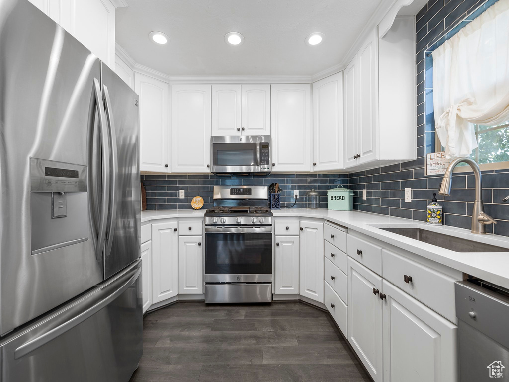 Kitchen with white cabinets, backsplash, dark wood-type flooring, appliances with stainless steel finishes, and sink