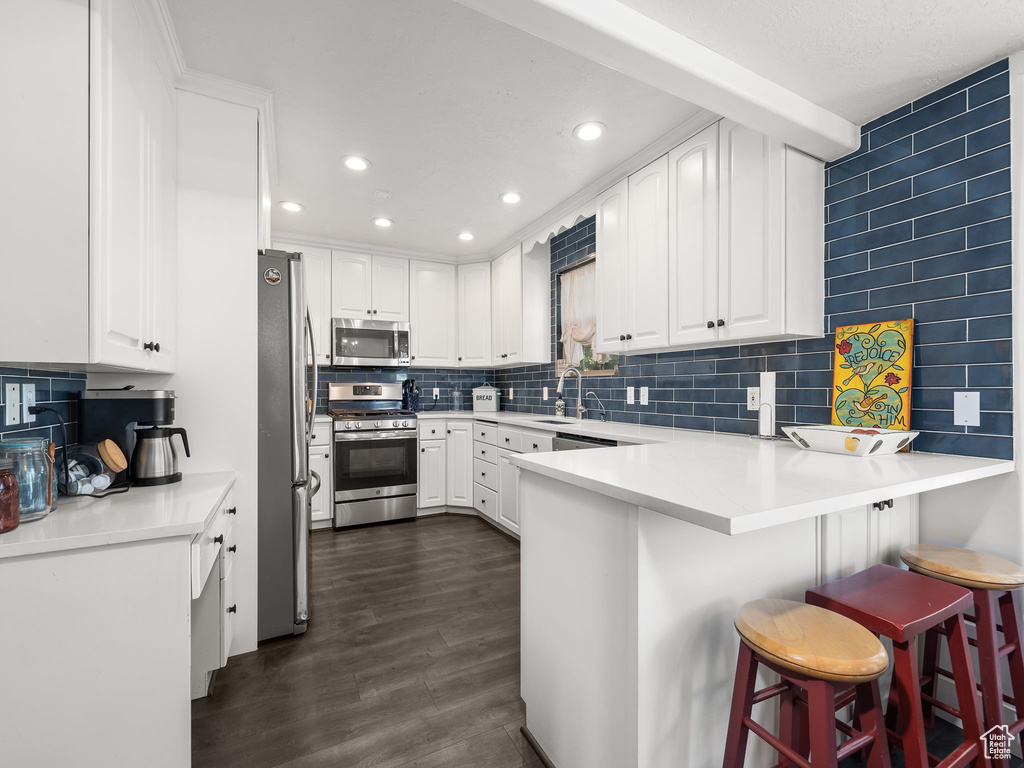 Kitchen with tasteful backsplash, a kitchen bar, white cabinetry, dark wood-type flooring, and appliances with stainless steel finishes