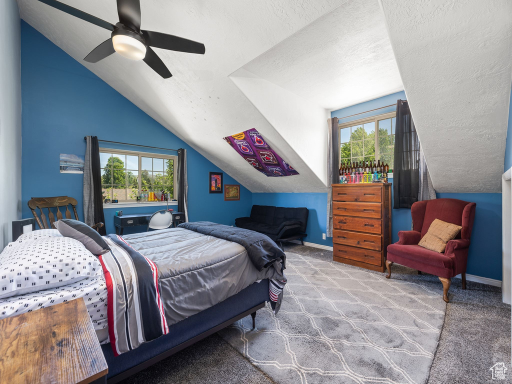 Carpeted bedroom featuring multiple windows, a textured ceiling, ceiling fan, and vaulted ceiling