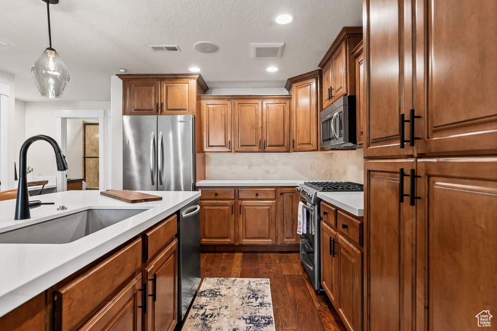 Kitchen with decorative light fixtures, dark hardwood / wood-style floors, tasteful backsplash, appliances with stainless steel finishes, and sink