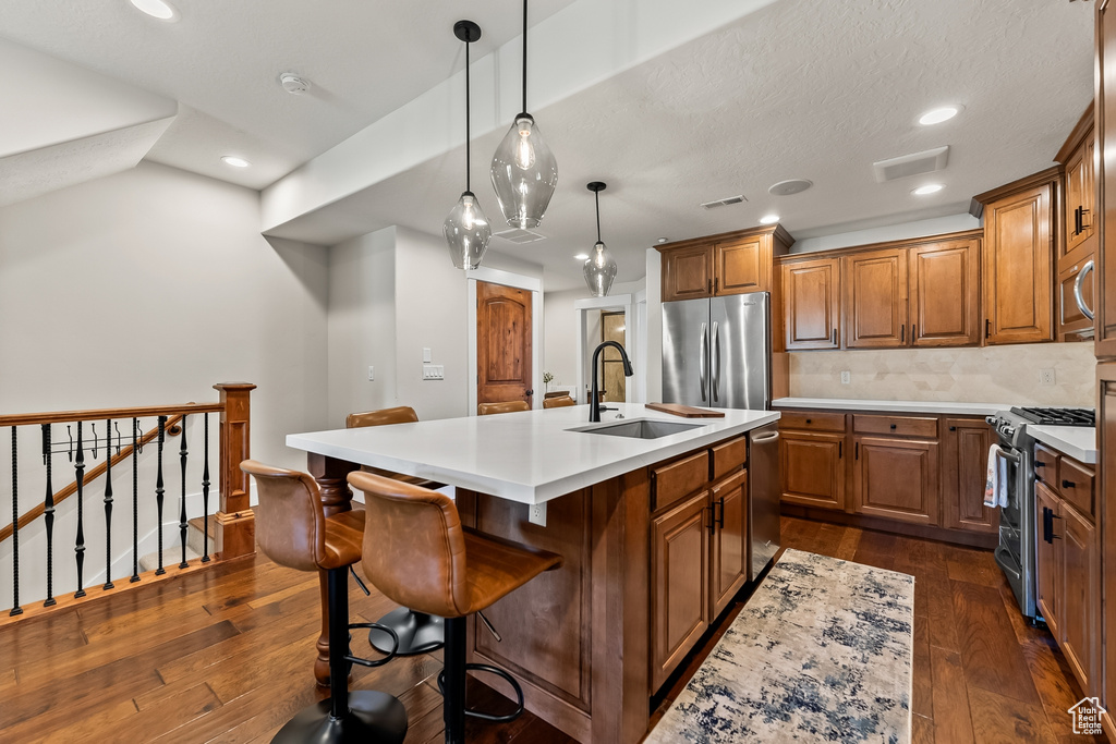 Kitchen featuring stainless steel appliances, dark hardwood / wood-style flooring, a center island with sink, and backsplash