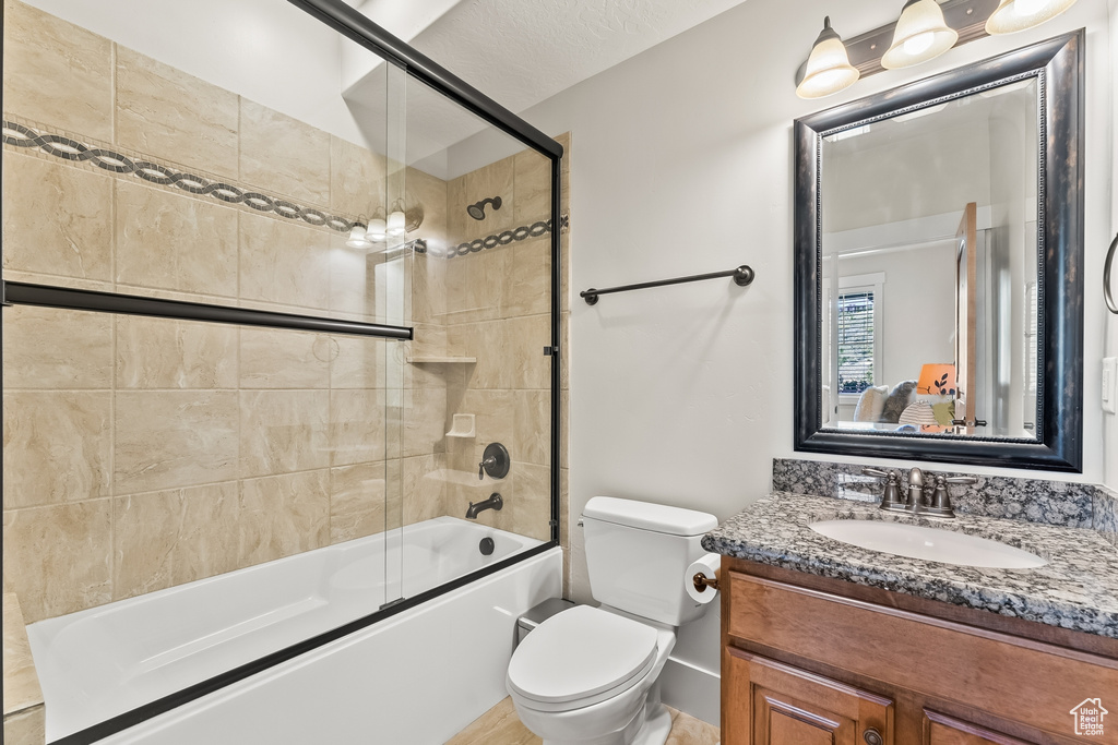 Full bathroom with combined bath / shower with glass door, vanity, toilet, and a textured ceiling