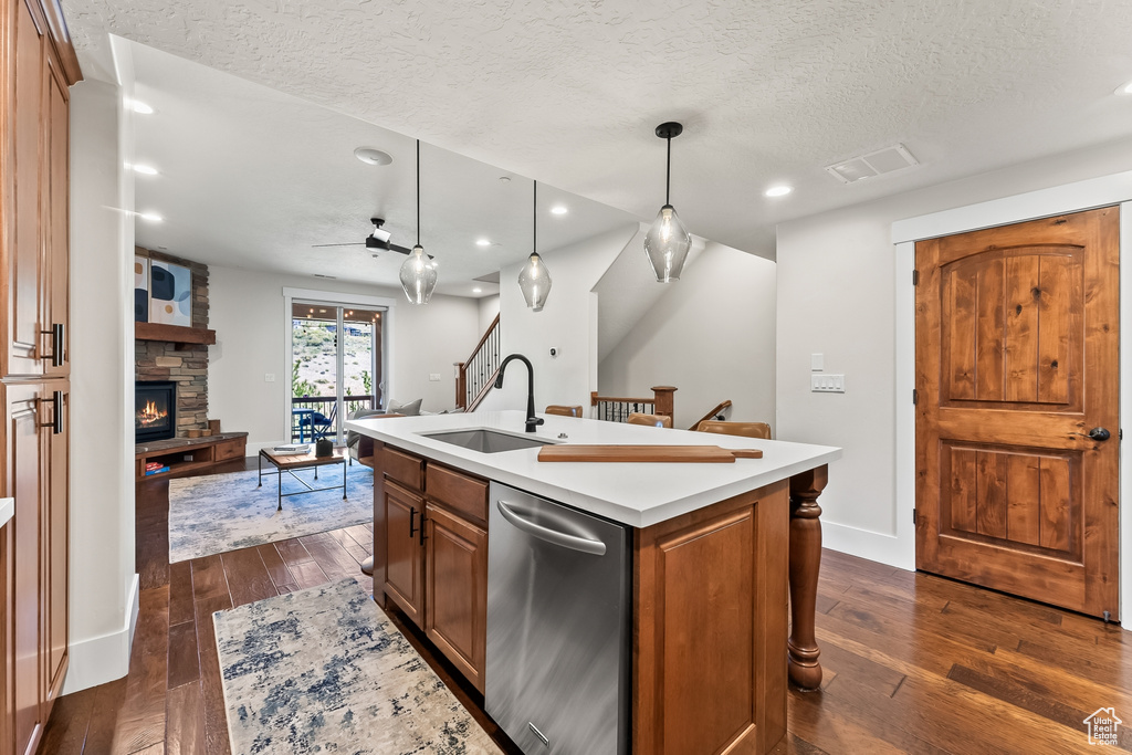 Kitchen with dark hardwood / wood-style flooring, dishwasher, a kitchen island with sink, a stone fireplace, and sink