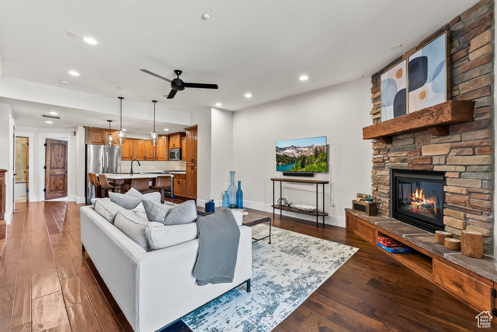 Living room with a stone fireplace, sink, ceiling fan, and dark hardwood / wood-style flooring