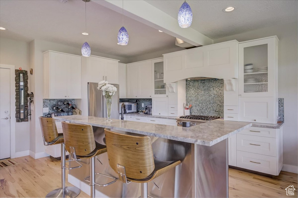 Kitchen with light hardwood / wood-style floors, backsplash, pendant lighting, and appliances with stainless steel finishes