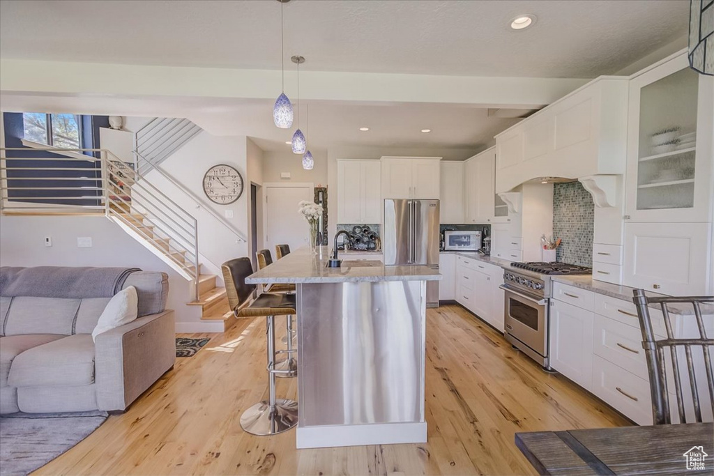 Kitchen with backsplash, high end appliances, white cabinetry, light wood-type flooring, and a breakfast bar