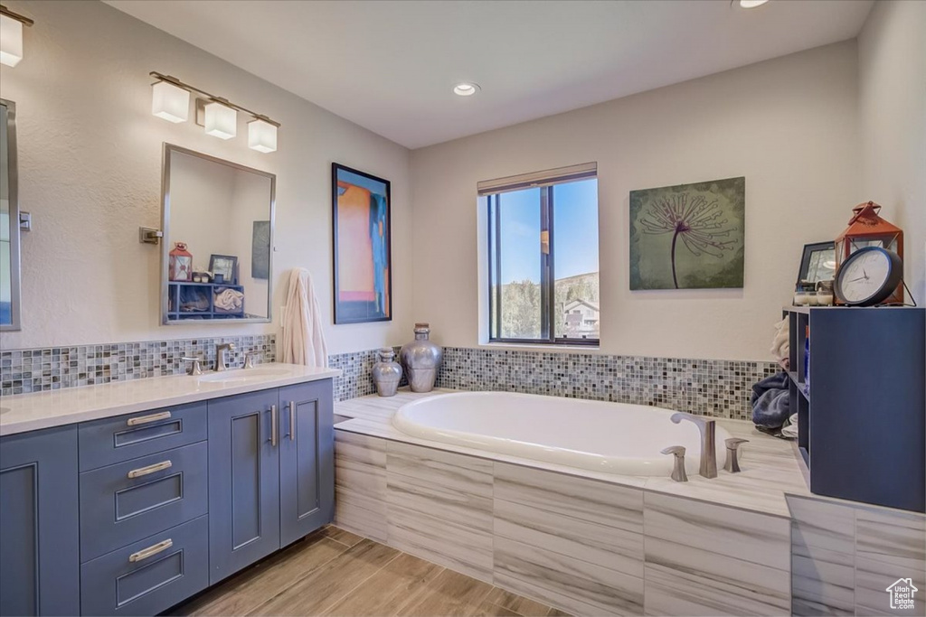 Bathroom with hardwood / wood-style flooring, tasteful backsplash, tiled bath, and vanity