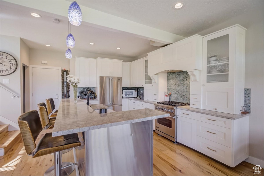 Kitchen with light hardwood / wood-style flooring, backsplash, a kitchen breakfast bar, white cabinetry, and premium appliances