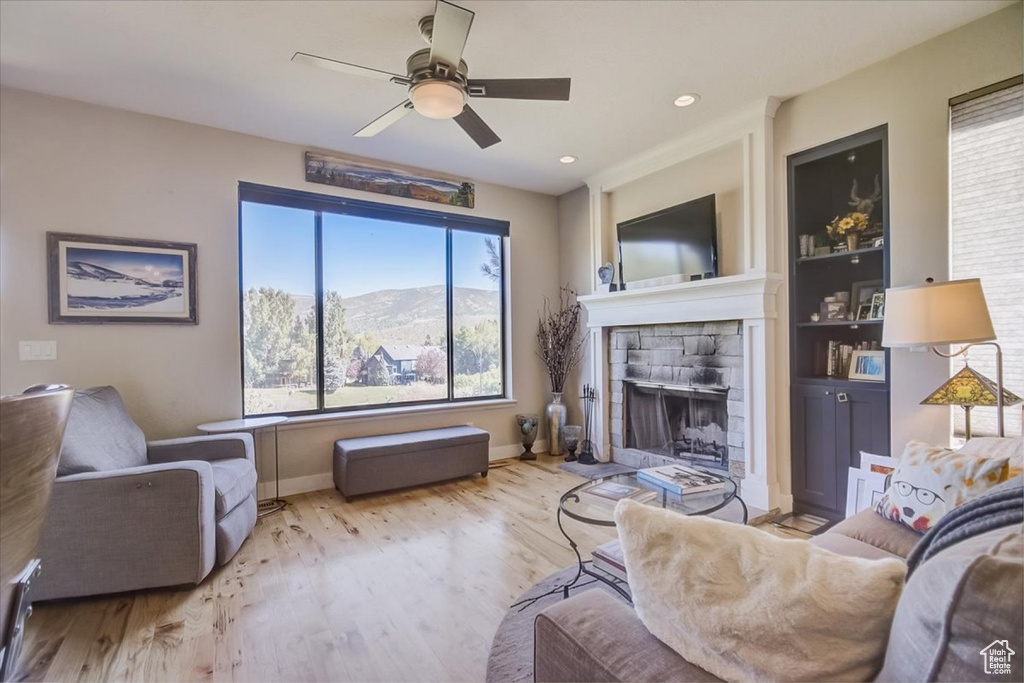 Living room with built in features, ceiling fan, a fireplace, and light wood-type flooring