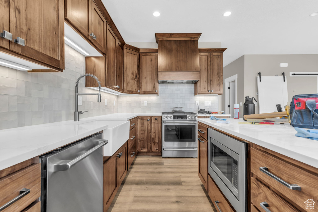 Kitchen with light hardwood / wood-style floors, appliances with stainless steel finishes, backsplash, sink, and custom exhaust hood