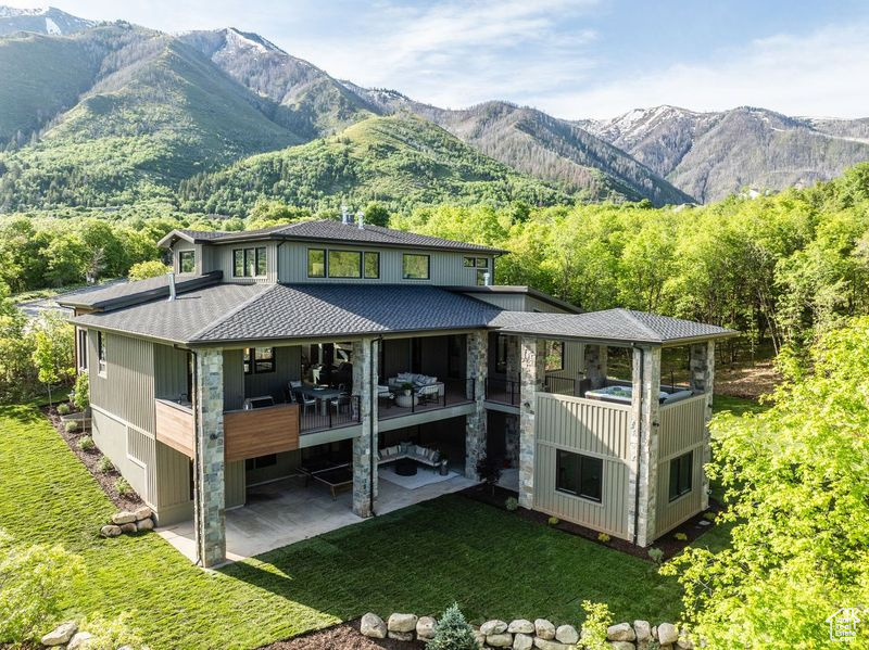 Back of house with a balcony, a lawn, and a mountain view