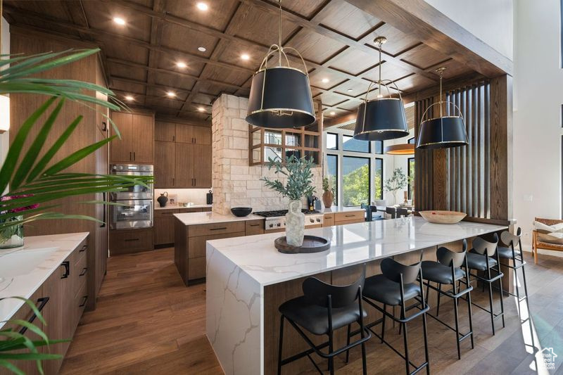 Kitchen featuring a large island, hardwood / wood-style flooring, coffered ceiling, and a kitchen bar