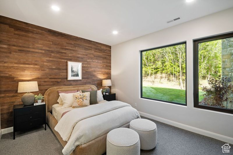 Carpeted bedroom featuring multiple windows and wood walls