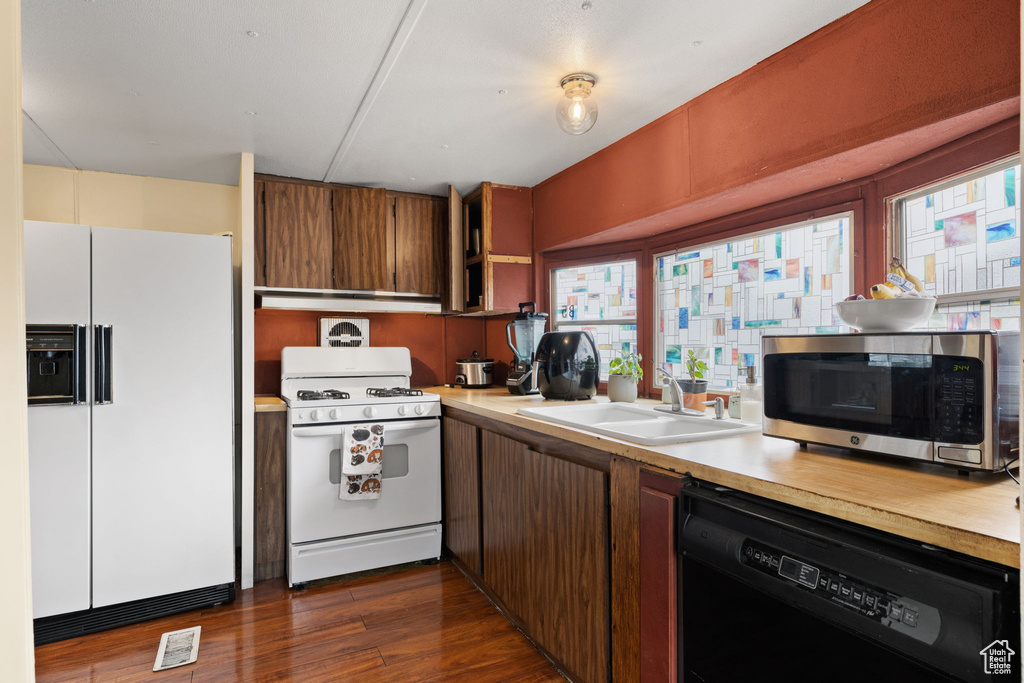 Kitchen with sink, plenty of natural light, white appliances, and dark hardwood / wood-style floors